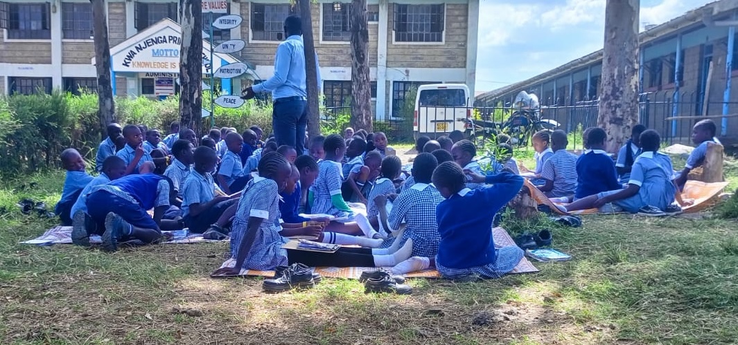 School kids sitting outside on the ground learning about hydroponics